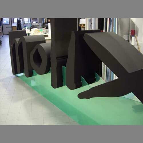 Lettere polistirolo verniciate Molix da 40 cm, dipinte di nero. Supporto a rampa in plexiglass trasparente dove sono fissate le lettere.